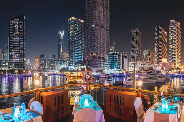 Dinner tables on a traditional dhow cruise overlooking the illuminated marina skyline