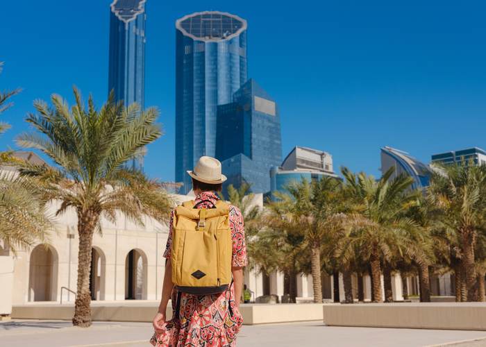 Traveller with a backpack arriving in Abu Dhabi, city towers behind her