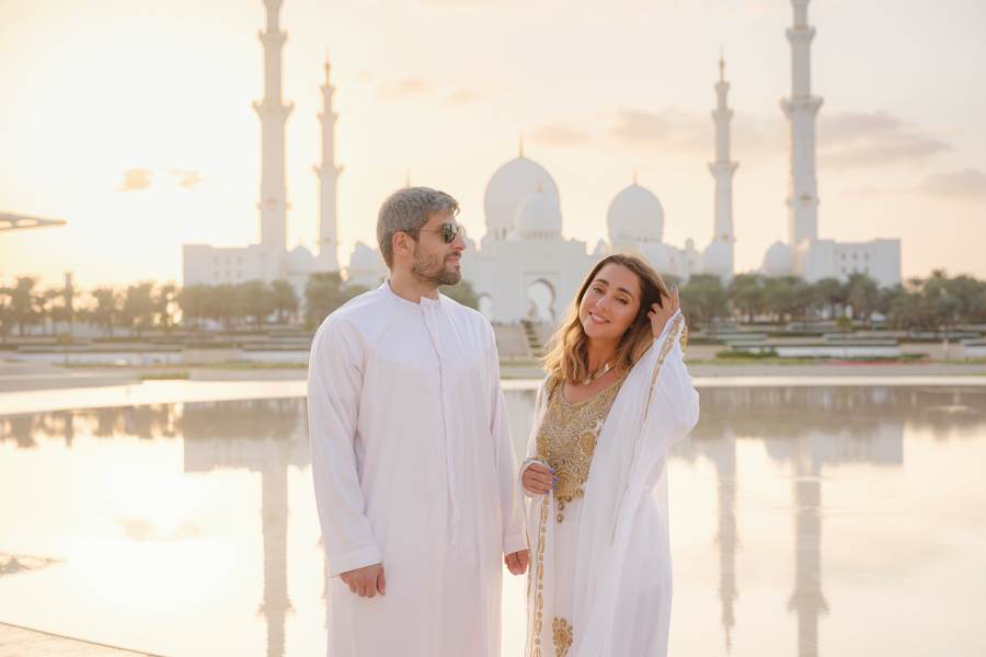 Couple in traditional dress in front of Sheikh Zayed Grand Mosque at sunrise