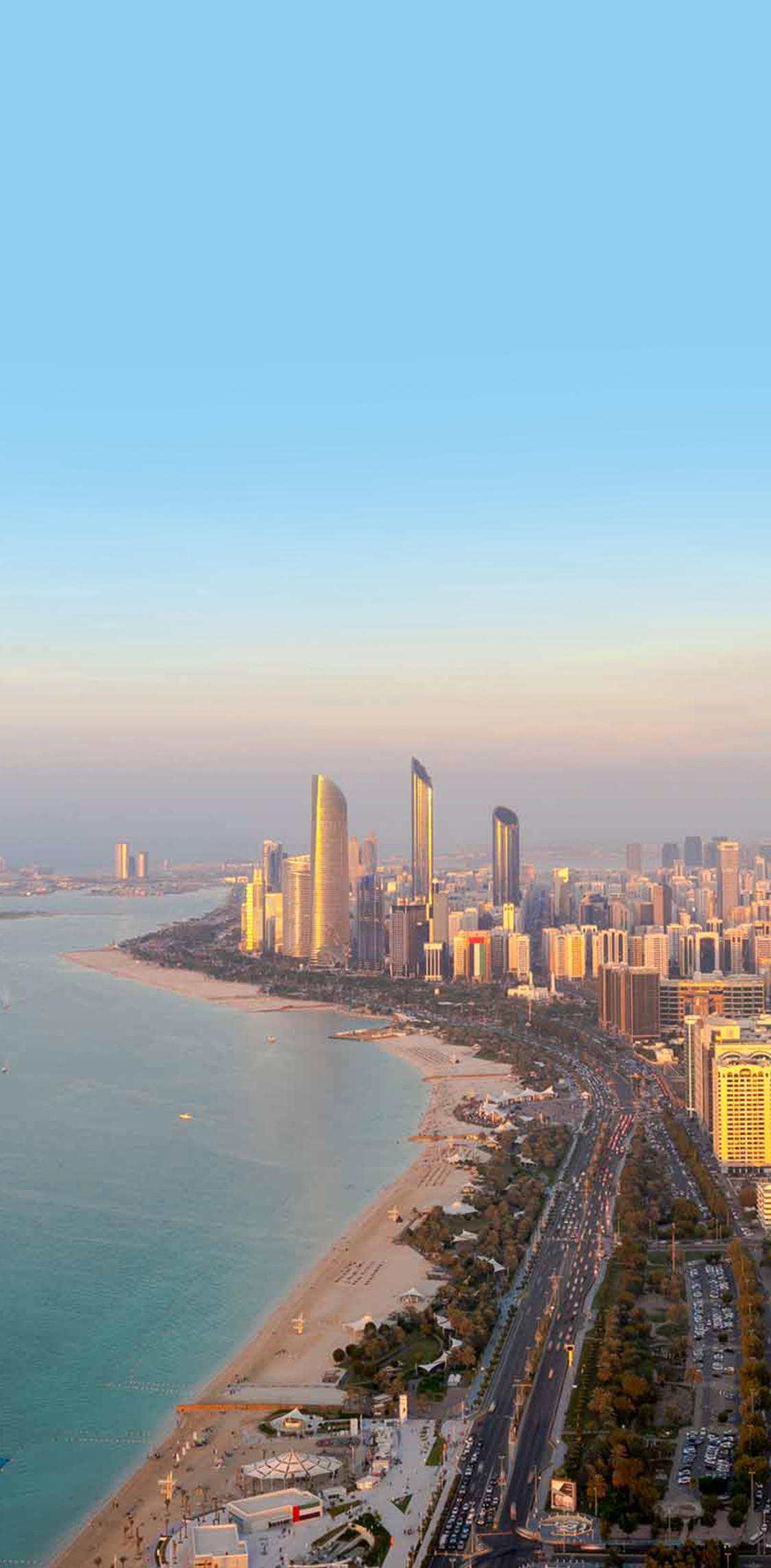 An aerial view of A'l Bahar Beach in Abu Dhabi, showcasing the scenic coastline, modern skyscrapers, and urban landscape stretching along the waterfront during a clear, serene evening.